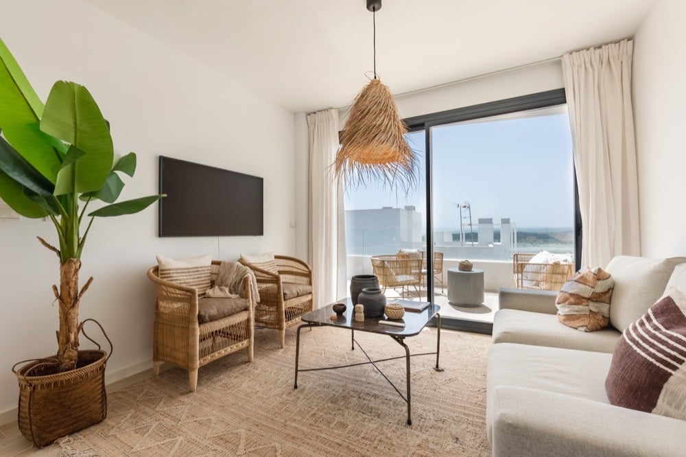 A condo-style suite living area with a sofa, coffee table, and balcony doors open to daylight.