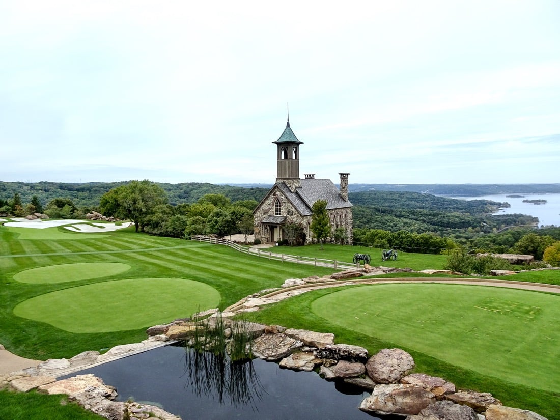 A stone chapel tower overlooking a manicured golf green and lake.