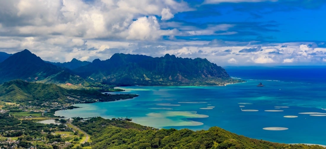 Aerial view of a turquoise Hawaiian bay below steep green ridges.
