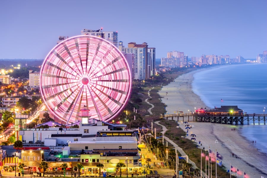 The SkyWheel lit pink above the Myrtle Beach shoreline and pier at dusk.