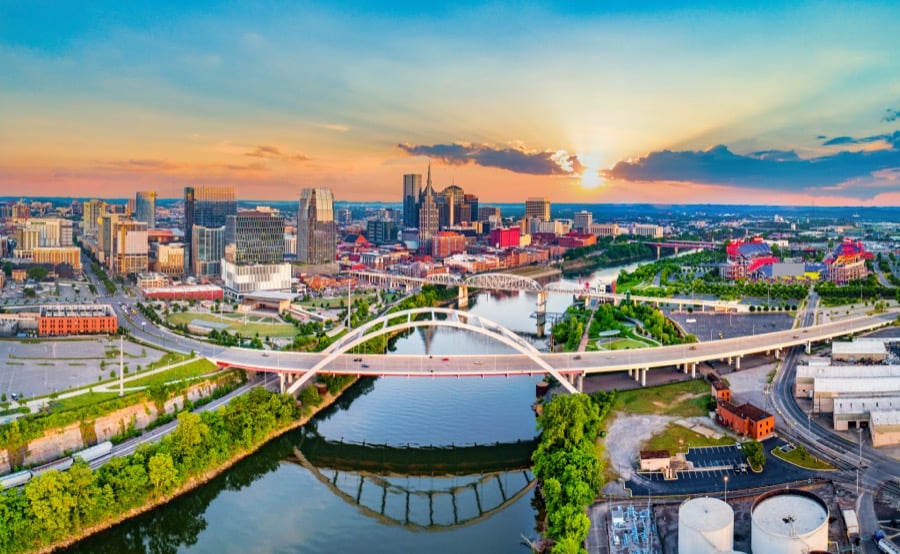 The Nashville skyline at sunset beyond the river and a pedestrian bridge.