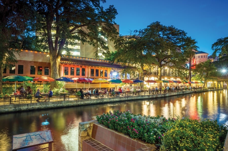 The San Antonio River Walk lit up at dusk along the tree-lined canal.