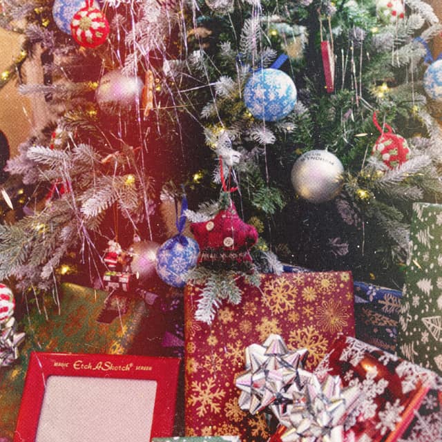 Wrapped gifts and an Etch A Sketch under a Christmas tree hung with ornaments and tinsel