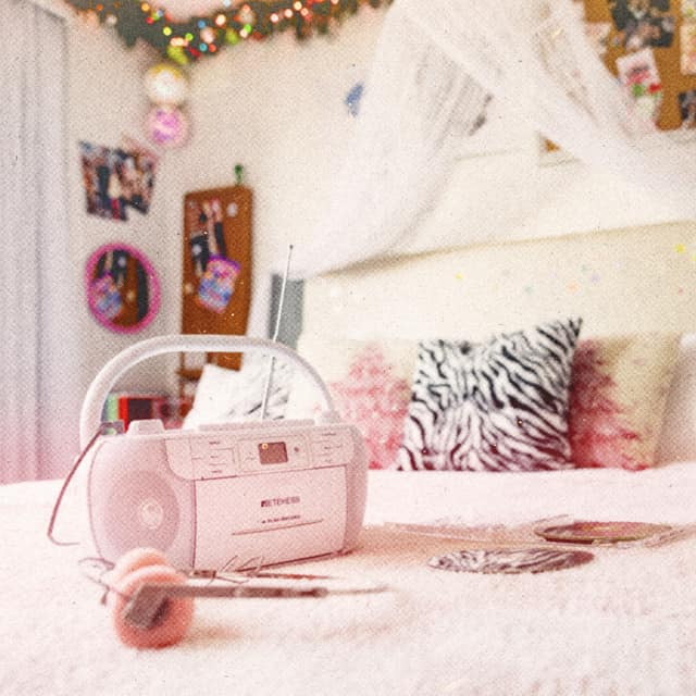 A bed with a zebra-print pillow and a pink boombox and headphones, under string lights