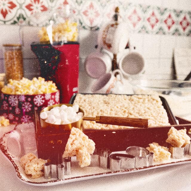 A tray of Rice Krispies treats, marshmallows, and popcorn tins on a holiday kitchen counter